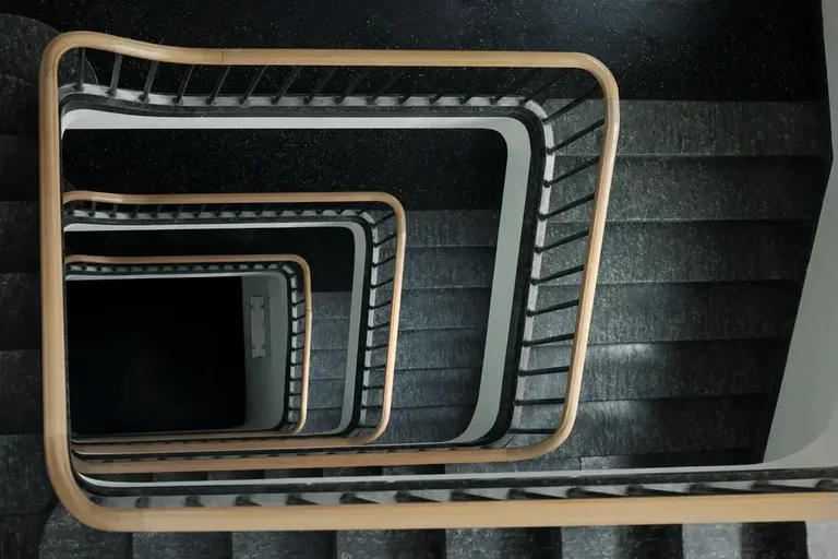 Treppenhaus im Vitus-Areal Winterthur von oben fotografiert mit spiralförmig angeordneten Stufen und Holzhandlauf.